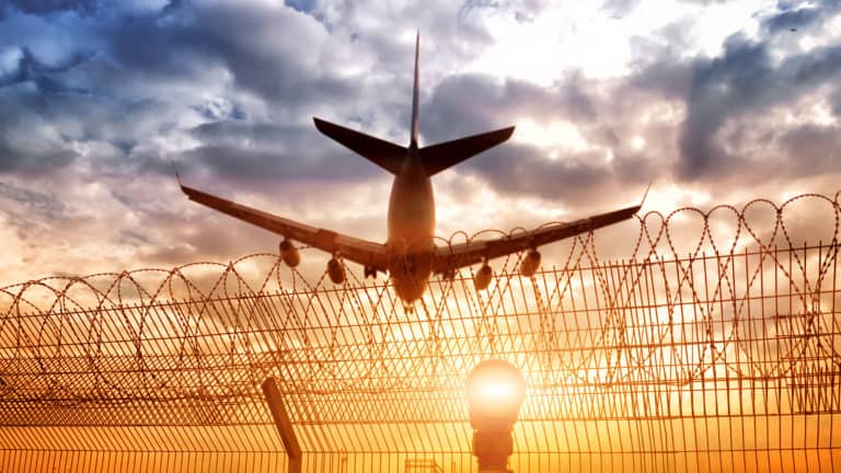 Airline flying over with sunset in background and fence in foreground